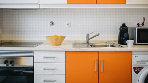 Et køkken med hvide og orange skabe, en stålvask, en mikrobølgeovn, en kaffemaskine og en vaskemaskine.