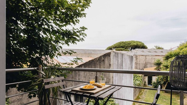 En balkon med et bord dækket til to personer, en potteplante og udsigt over bybilledet.