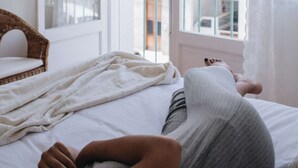 Et soveværelse med en seng, en fletstol og udsigt til en balkon med bygninger i baggrunden.