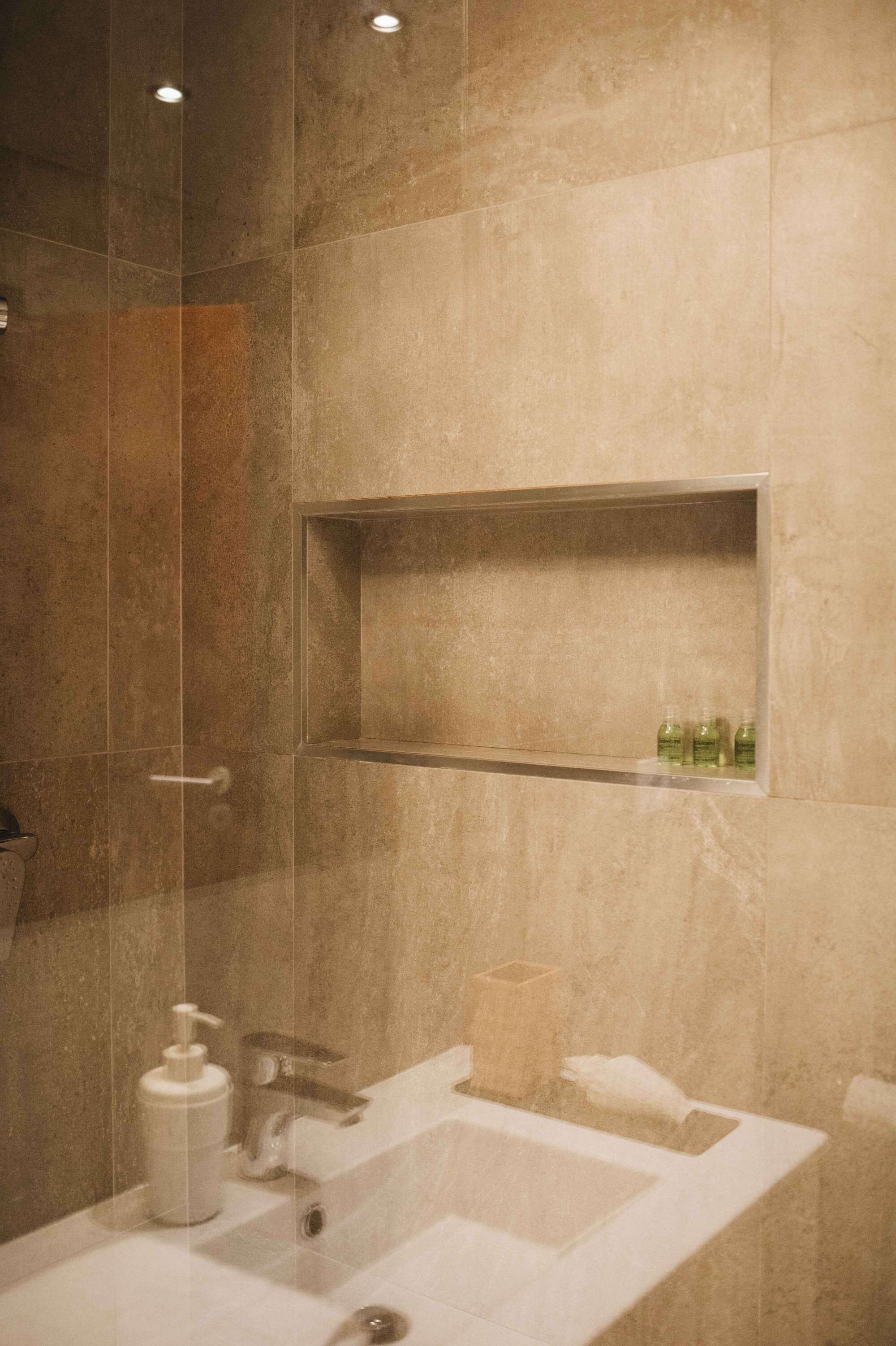 A modern bathroom with a glass-enclosed shower, a white sink, and a shelf with toiletries.