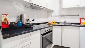 Uma cozinha moderna com armários brancos, bancada preta, forno embutido, máquina de café e pia.