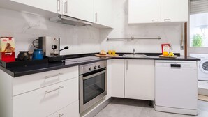 Cozinha moderna com armários brancos, bancada preta, forno embutido, lava-louças e janela que traz luz natural.