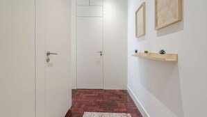 Een gang met een houten vloer, een witte deur en een wandplankje met kleine planten.