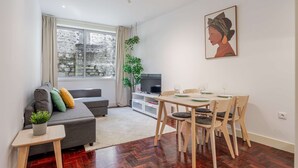 Een moderne woonkamer met een grijze bank, een eettafel voor vier personen en een televisie op een witte kast.