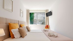 Een hotelkamer met een groot bed, een flatscreen televisie aan de muur, een raam met gordijnen en een nachtkastje met een lamp.