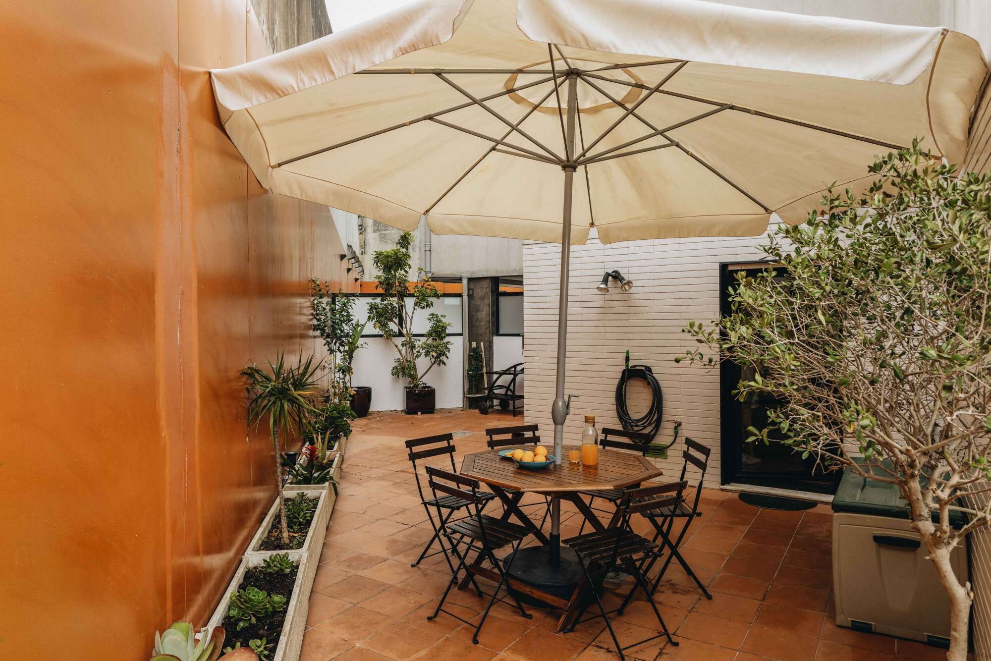 An outdoor patio with a round table and chairs, a large umbrella, and potted plants.