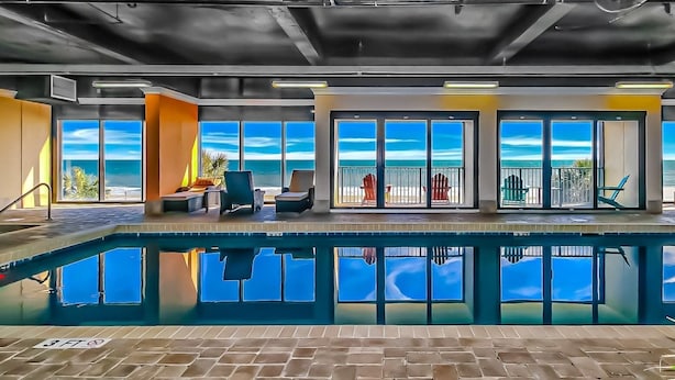 A pool area with a view of the ocean, a lounge with chairs, and a door leading to a balcony.