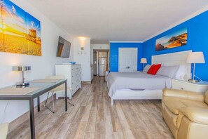Una habitación de hotel con cama, escritorio, silla, sofá y obras de arte en las paredes.
