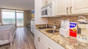 A hotel room with a balcony, a bed, a kitchenette with a sink, and a microwave.