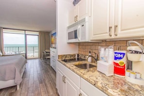 A hotel room with a balcony, a bed, a kitchenette with a sink, and a microwave.