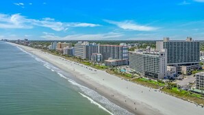 A coastal hotel with multiple high-rise buildings, a beach, and a clear blue sky.
