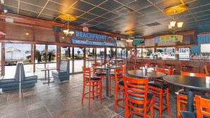 A beachfront restaurant with outdoor seating, a bar, and a view of the ocean.