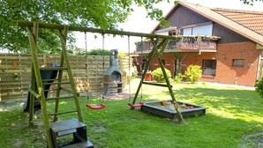 A backyard with a swing set, a playhouse, and a brick house. - Beach tent large - house beach shell / Biedrowski (Friedrichskoog)