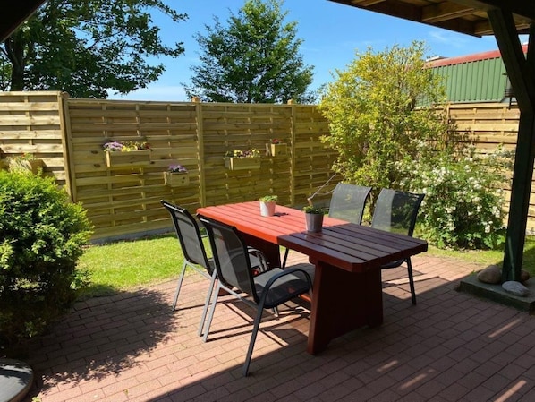 Une terrasse avec une table et des chaises en bois, une clôture en bois et de la verdure.