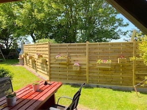 Une clôture en bois agrémentée de jardinières, une table rouge et une cour gazonnée.