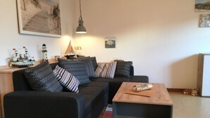 A living room with a sofa, a coffee table, a lamp, and a ship model on a side table. - Beach tent large - house beach shell / Biedrowski (Friedrichskoog)