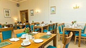 Une salle à manger d’hôtel avec de nombreuses tables et chaises, chacune mise avec des assiettes, des tasses et des couverts blancs.