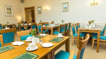Ein Hotel-Speisesaal mit mehreren Tischen und Stühlen, jeder Tisch gedeckt mit weißen Tellern, Tassen und Besteck.