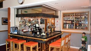 Un espace bar comprenant un comptoir, des tabourets et une variété de bouteilles et de verres.