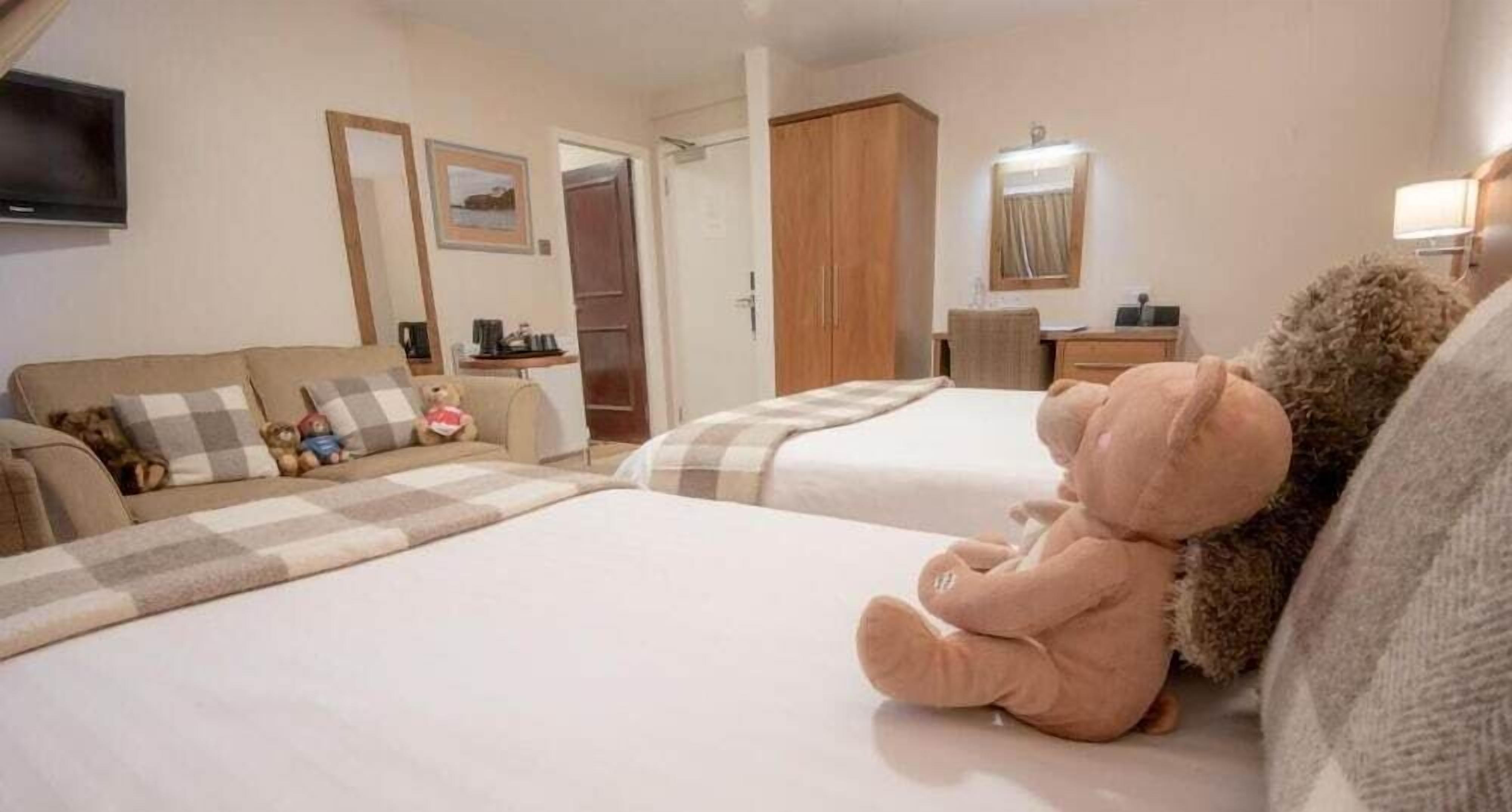 A hotel room with two beds, a sofa, a desk, and a television.