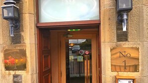 Une entrée d’immeuble avec une porte en bois, une enseigne au-dessus de la porte et deux appliques murales.
