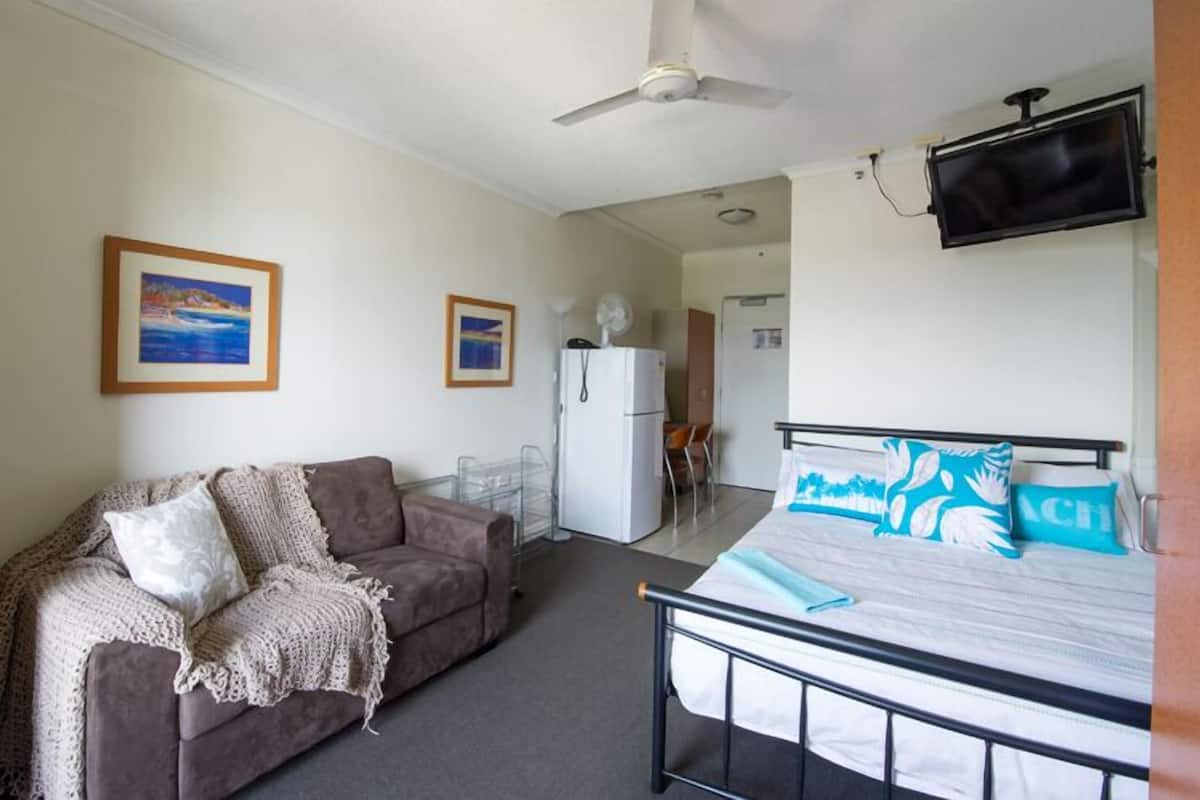 Une chambre avec un lit, un canapé, un ventilateur de plafond, une télévision et un réfrigérateur.