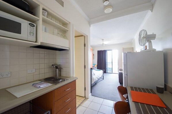 A compact kitchen with a microwave, stove, and cabinets, leading to a bedroom with a bed and a window. - Shaftson (Kangaroo Point)