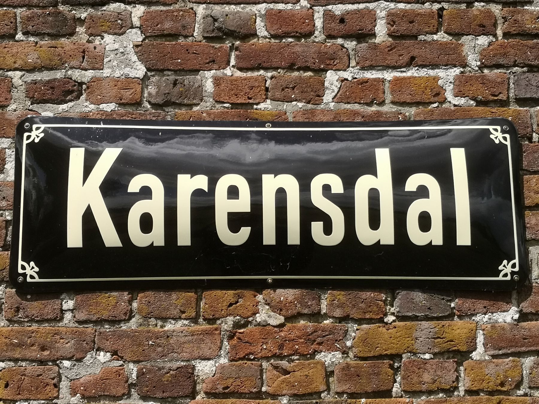 Un letrero negro con la palabra 'Karensdal' en letras blancas sobre un muro de ladrillo.