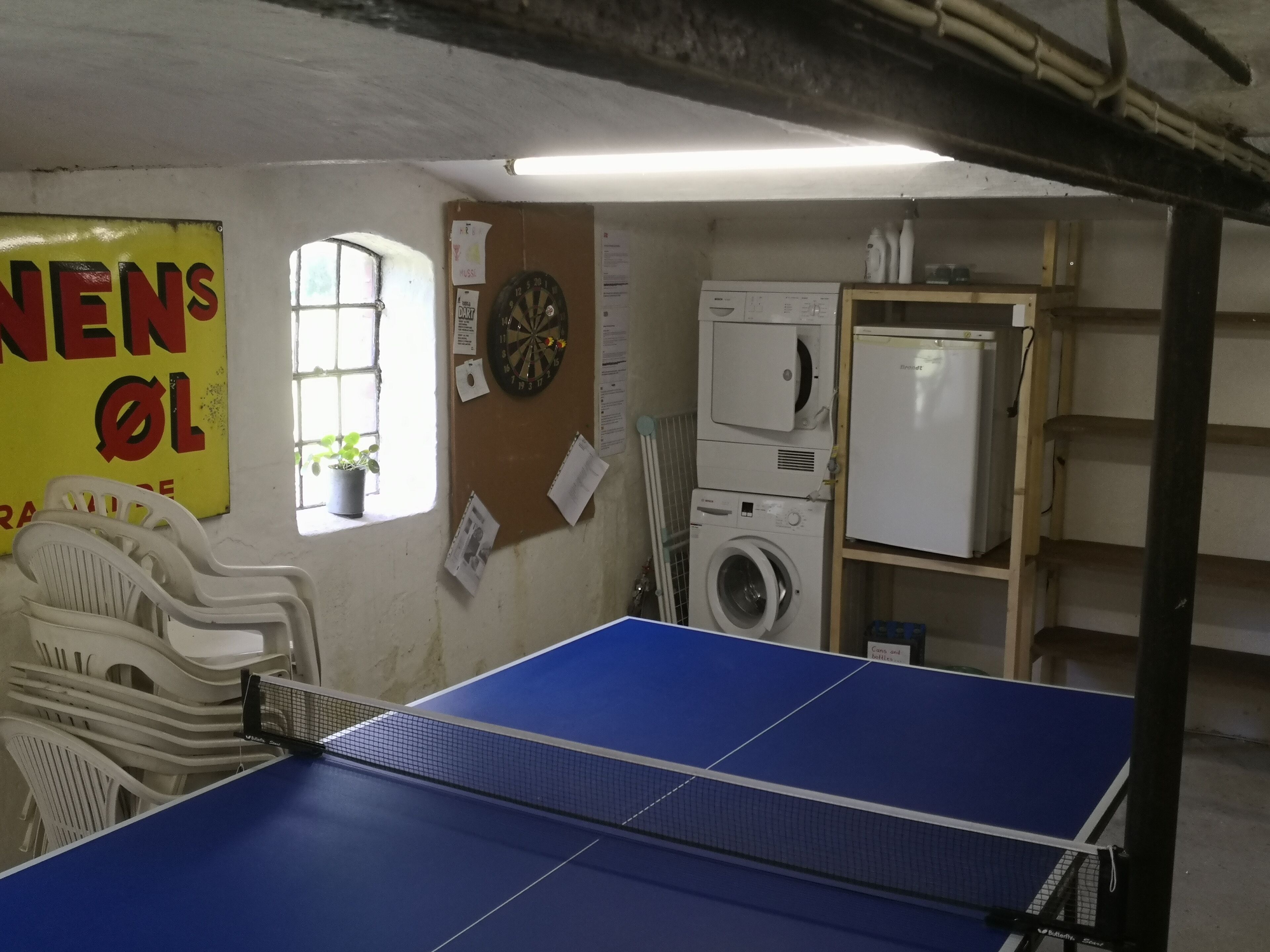 Una stanza con tavolo da ping pong, lavatrice, asciugatrice e bersaglio per freccette.