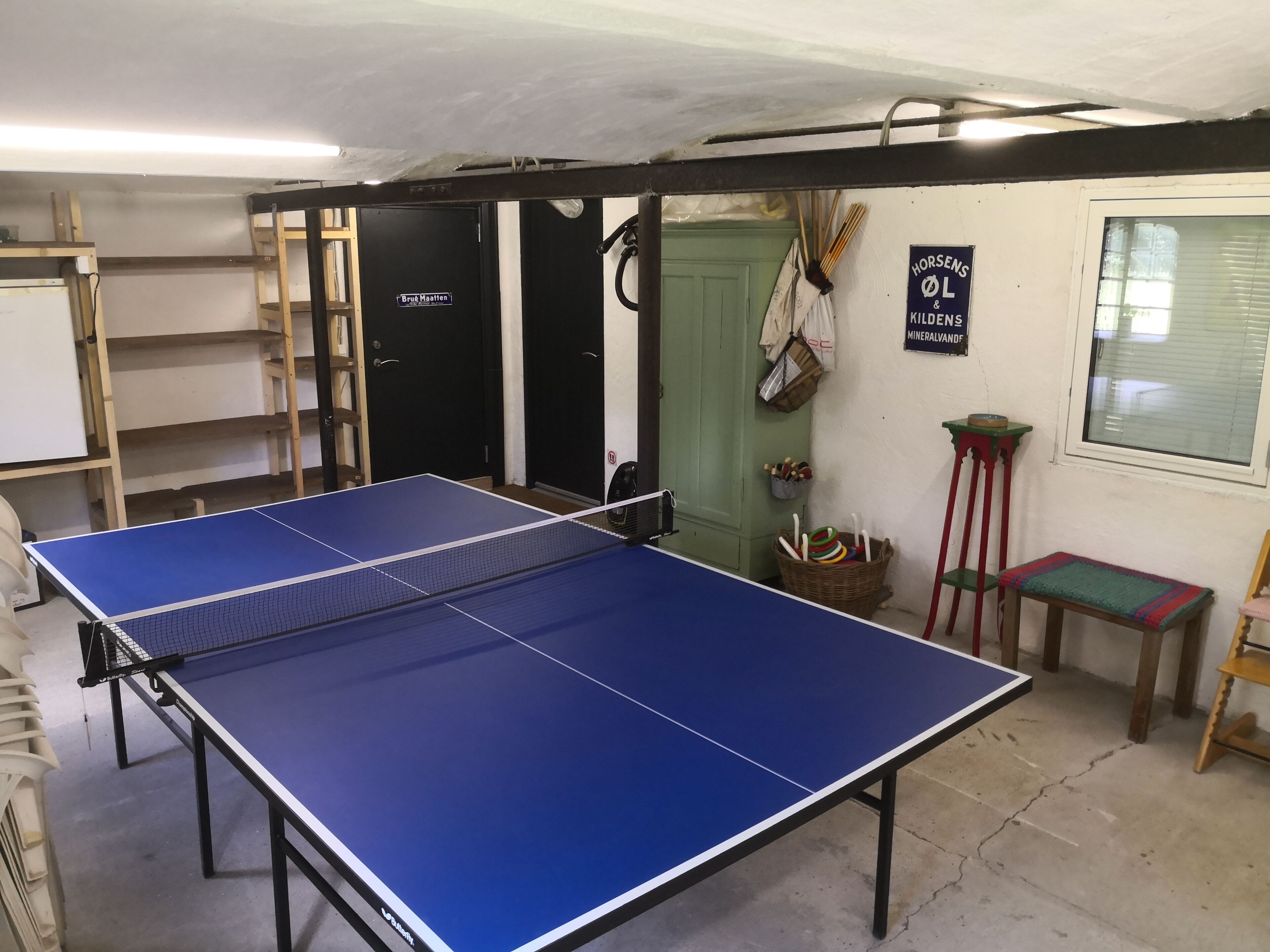 Une table de ping-pong se trouve dans une pièce avec une porte verte, une fenêtre et un panneau accroché au mur.