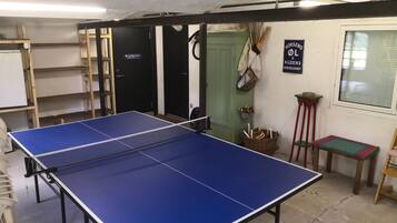 Une table de ping-pong se trouve dans une pièce avec une porte verte, une fenêtre et un panneau accroché au mur.