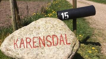 Une pierre sur laquelle est gravé le mot « KARENSDAL », un poteau noir portant le numéro « 15 », et un paysage rural avec des champs et un chemin de terre.