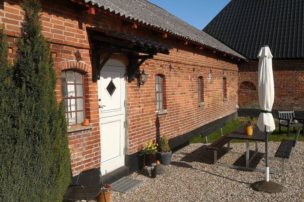 A brick building with a white door, windows, and a small garden area with a bench and table.