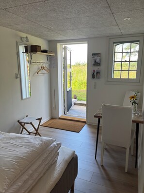 A bedroom with a bed, a desk, a chair, a window, and a door leading to an outdoor area. - Karensdal B & B (Uldum)
