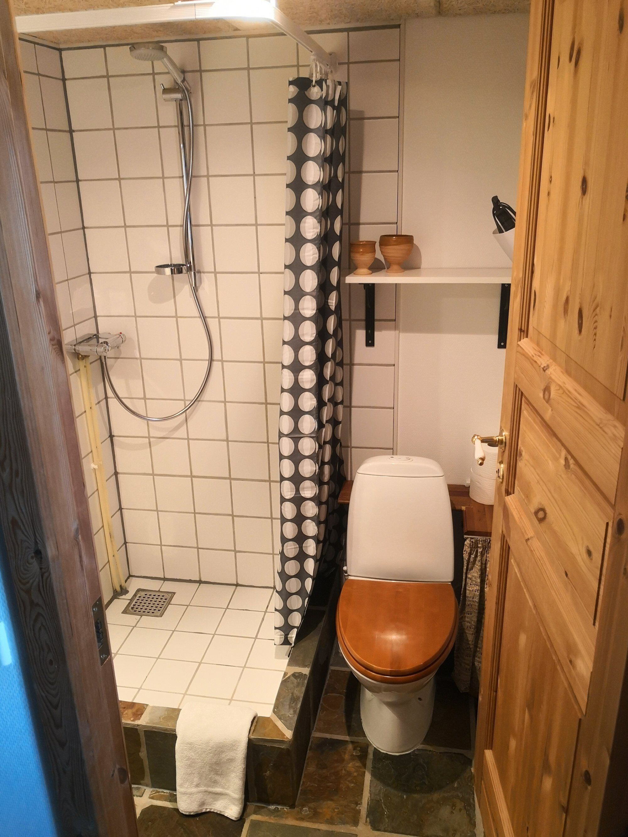 A bathroom with a shower, toilet, and a shelf with two bowls.