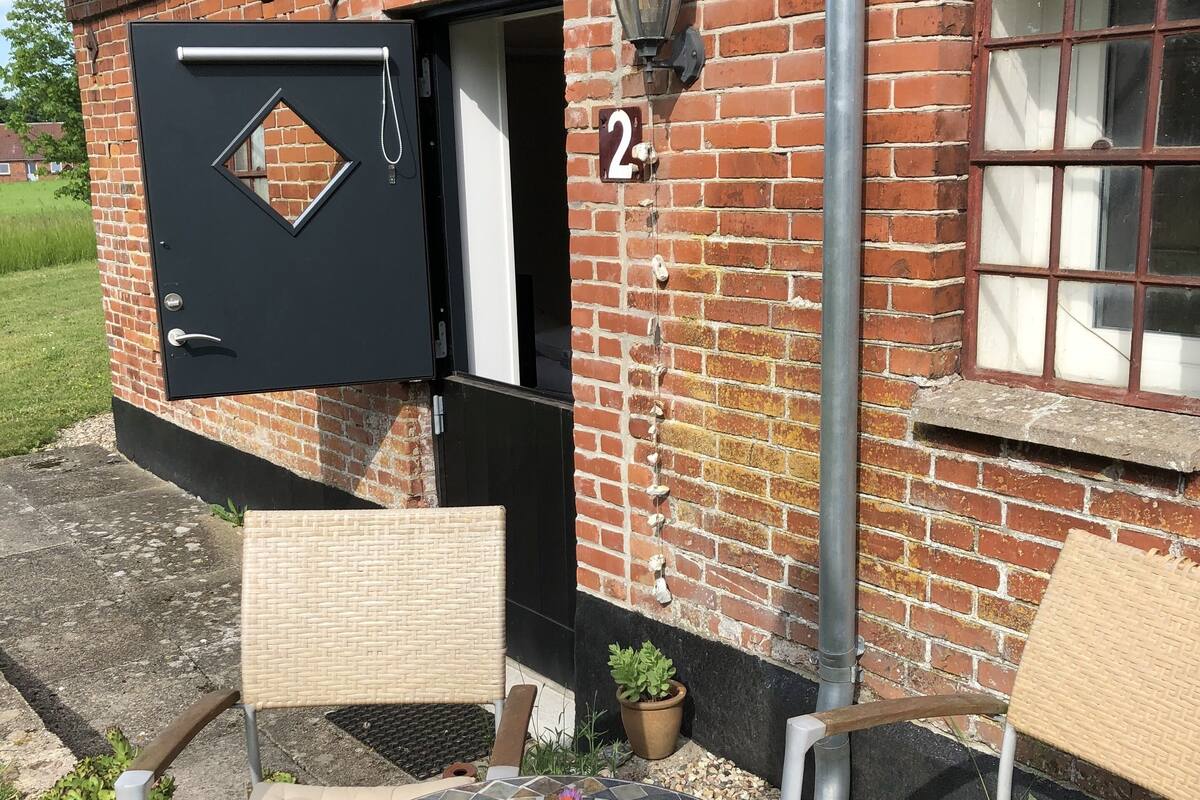 A brick building with a black door, numbered 2, and a small table with chairs and a potted plant.