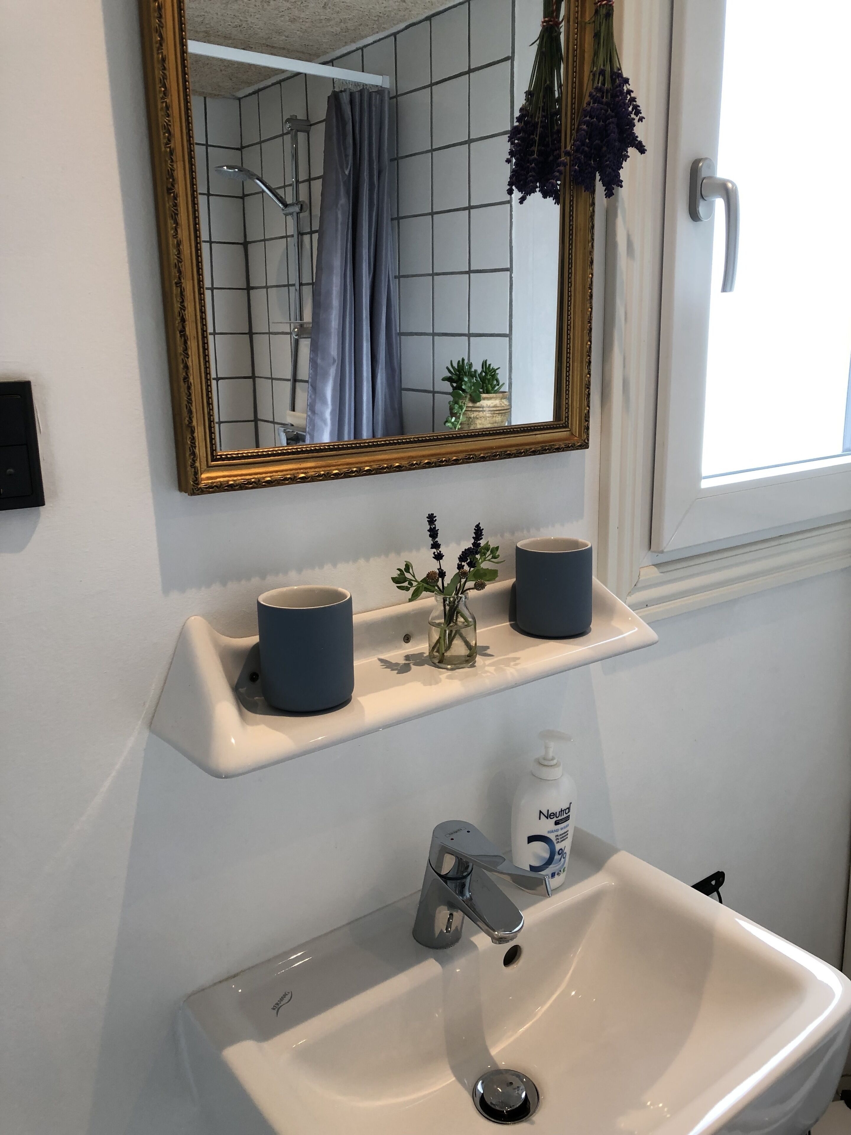 A bathroom with a white sink, a mirror with a gold frame, and a window with a view of the outside.