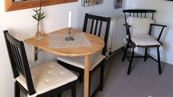 A small dining area with a wooden table and two chairs, a candle, and a vase with a plant.