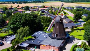 A windmill with a modern extension, surrounded by residential houses and green fields.