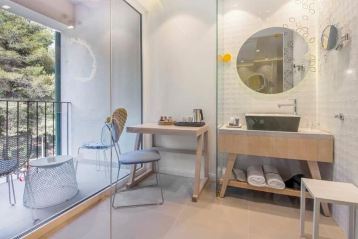 A modern bathroom with a glass partition, a round mirror, a wooden vanity, and a small table with chairs.