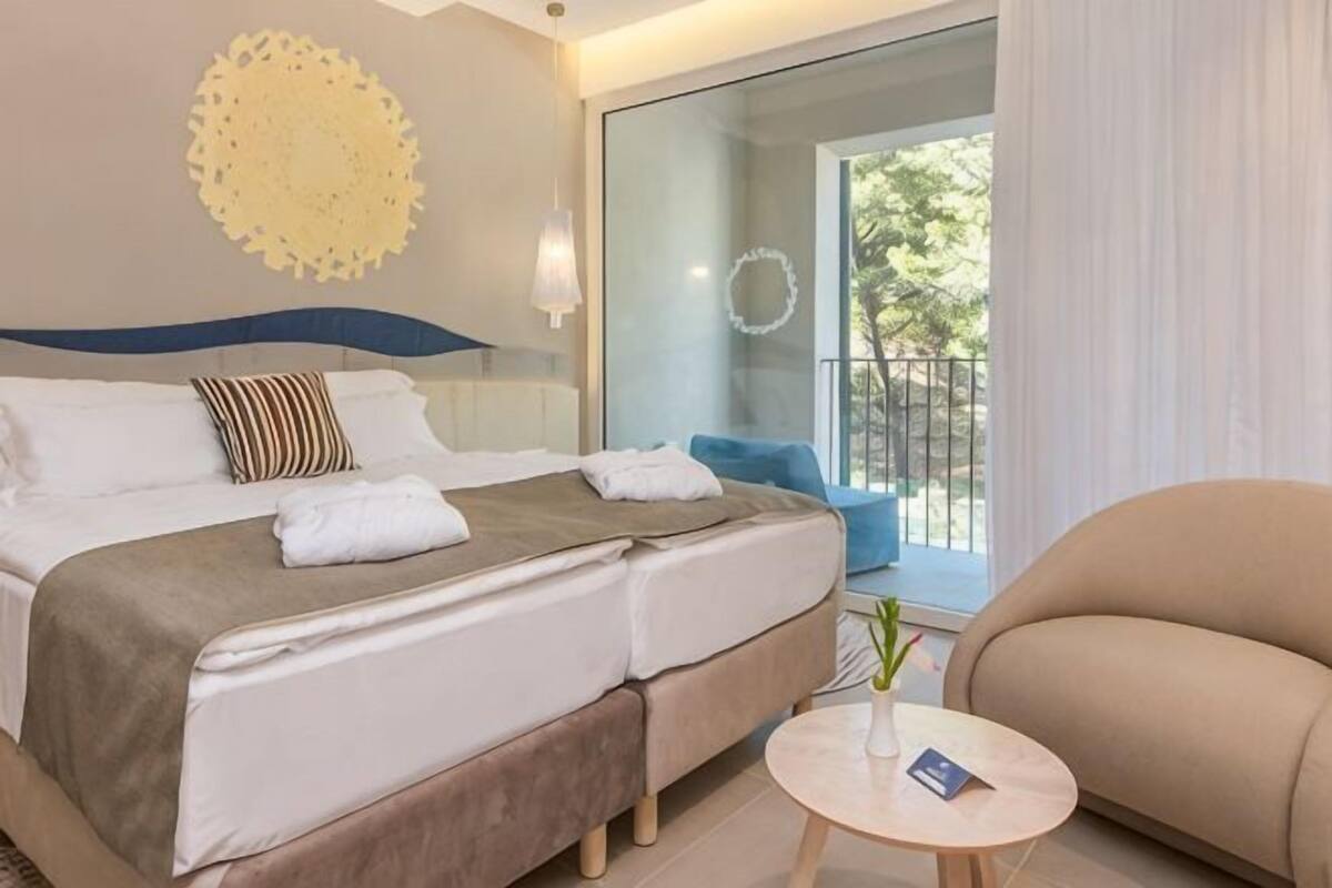 A hotel room with a bed, a small round table, a sofa, and a view of the outdoors.