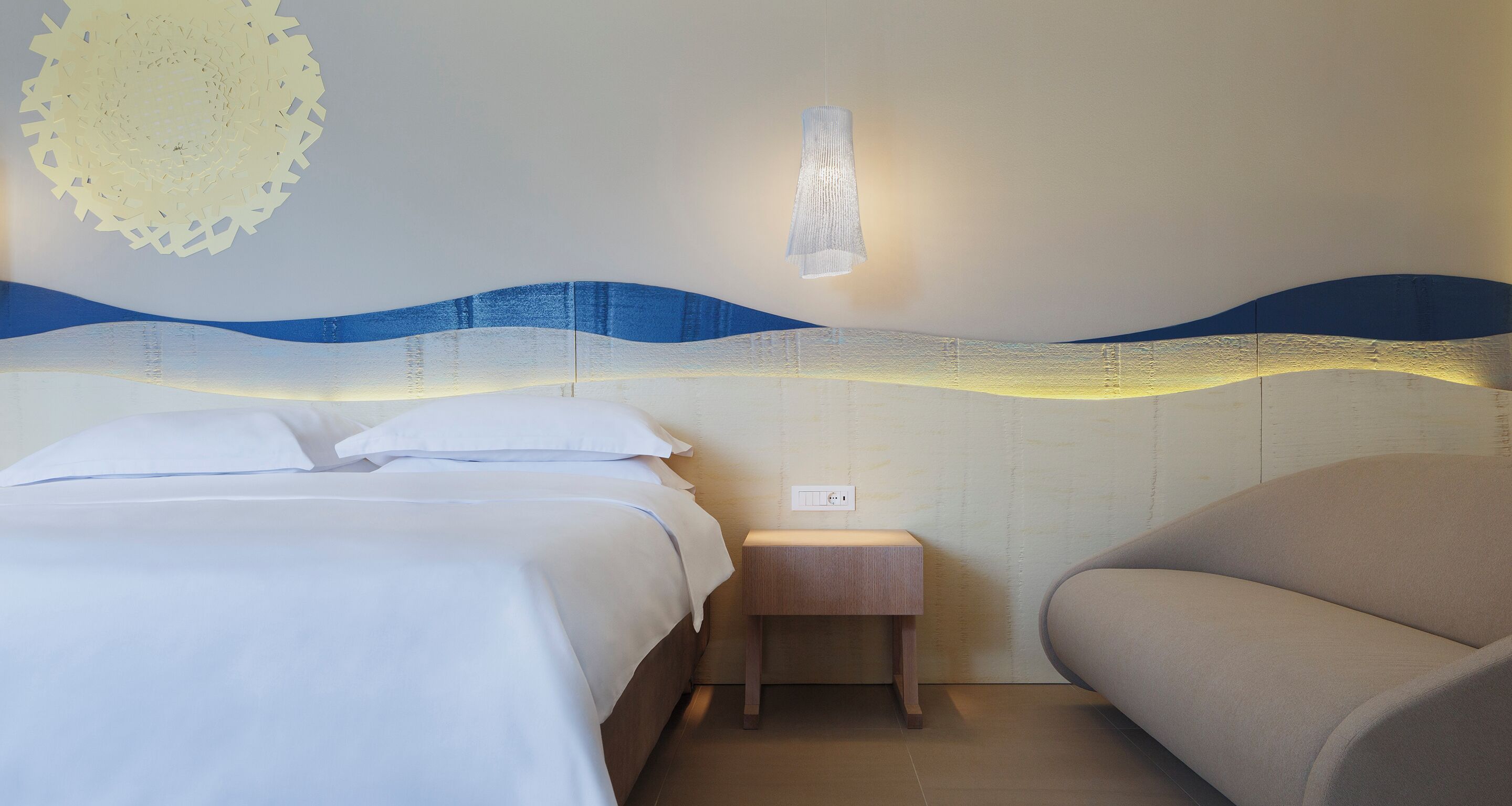 A hotel room with two beds, a nightstand, a lamp, and a wall with a wave-like design.