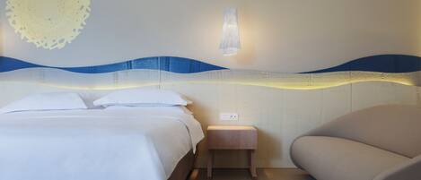 Habitación de hotel con dos camas, una mesita de noche, una lámpara y una pared con diseño ondulado.