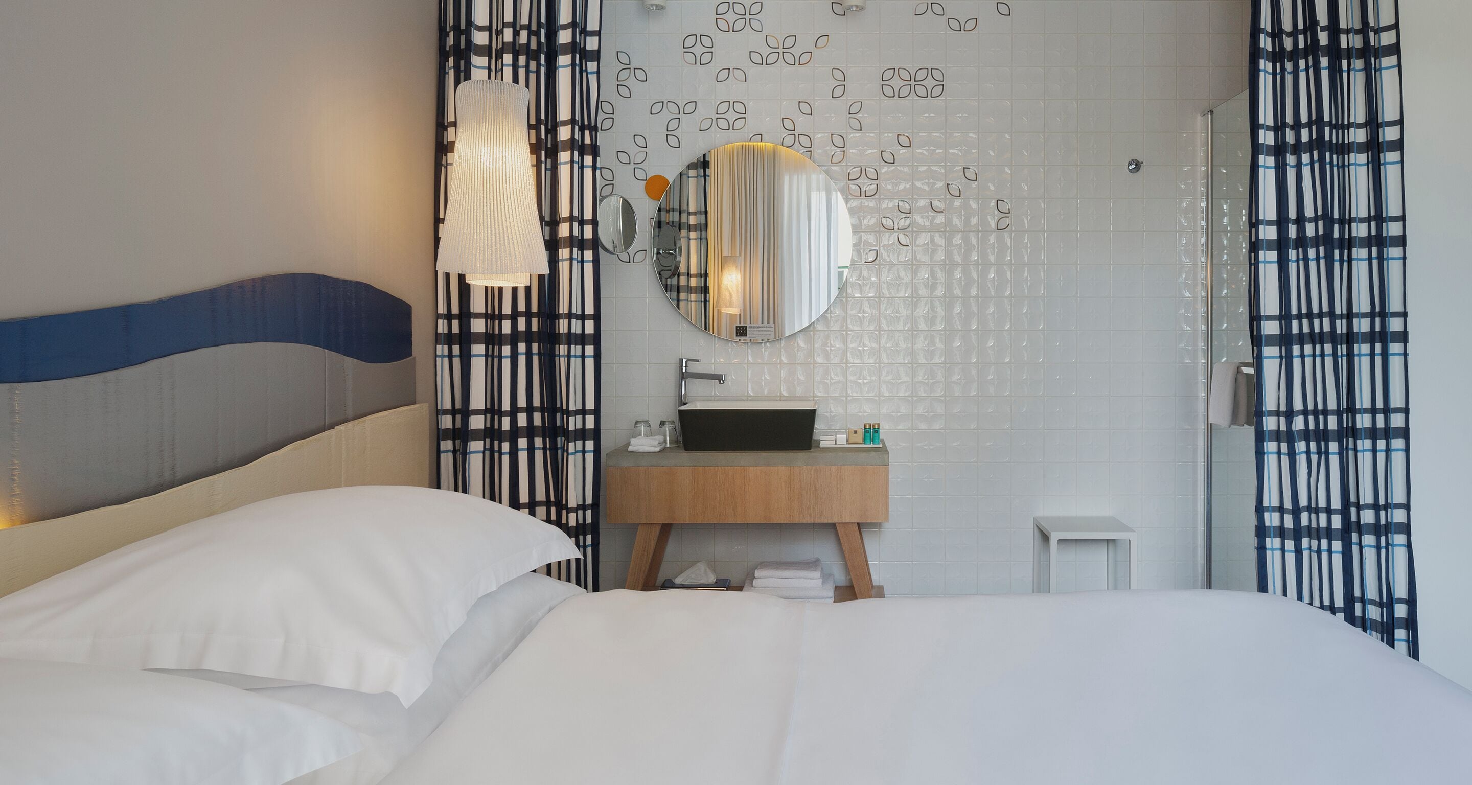 Une chambre d’hôtel comprenant un lit, une table de chevet, un miroir, un lavabo et un espace douche.