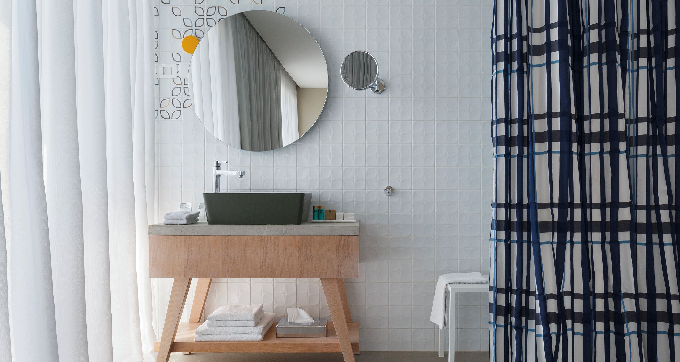 Une salle de bain moderne avec un miroir rond, un lavabo et une étagère en bois où sont posées des serviettes.