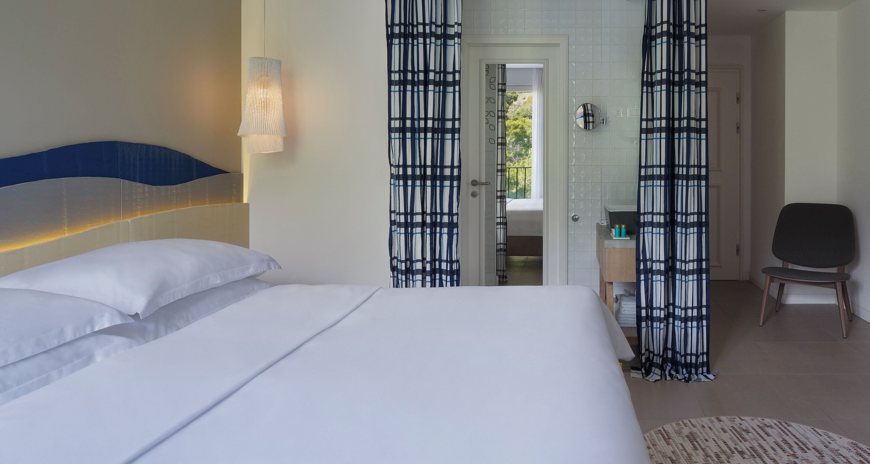 Une chambre d’hôtel avec un grand lit, une chaise, une salle de bain avec un miroir et une vue sur l’extérieur.