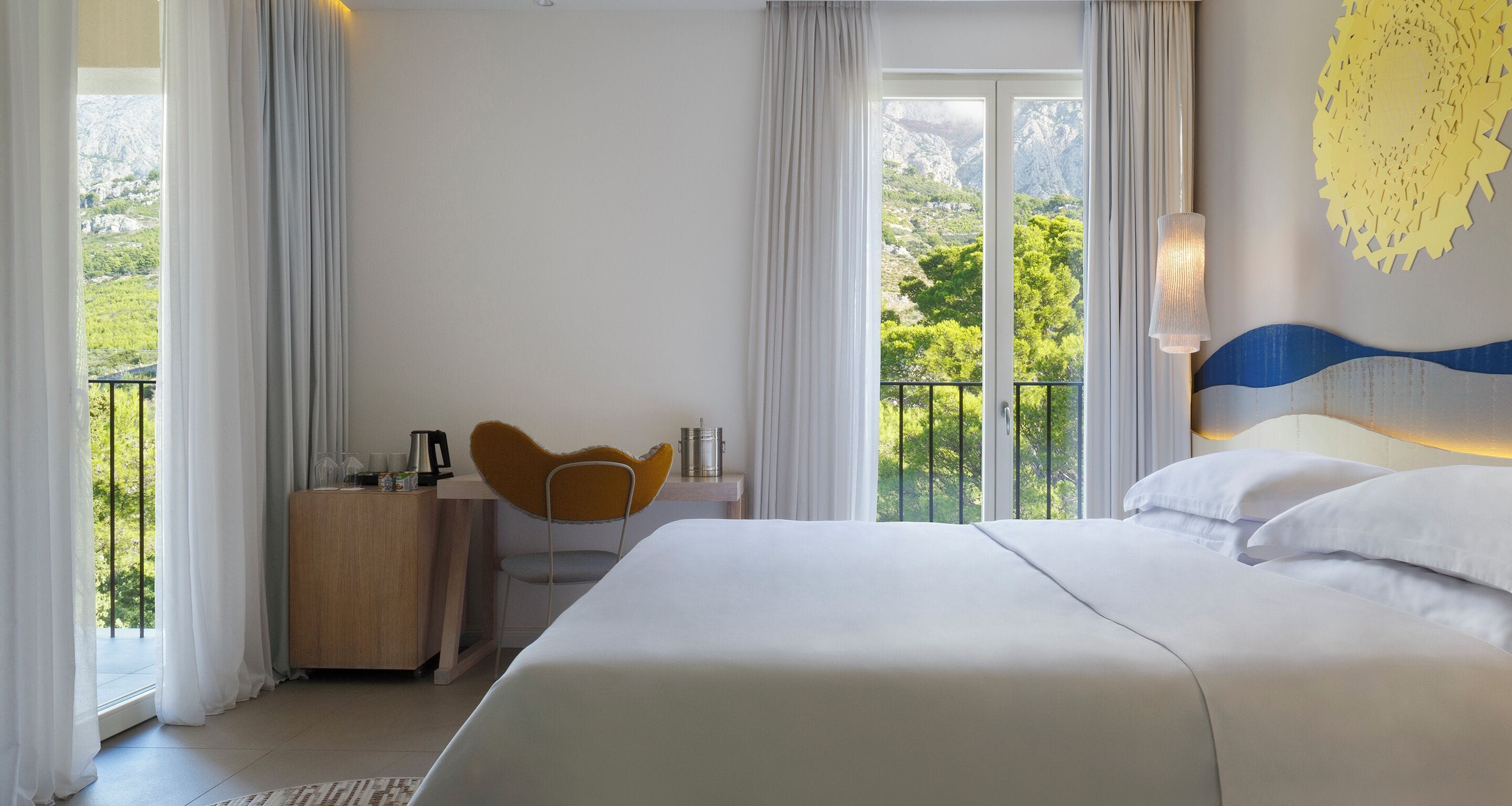 Une chambre d’hôtel avec un lit, un bureau et une chaise, une vue sur l’extérieur et un balcon.