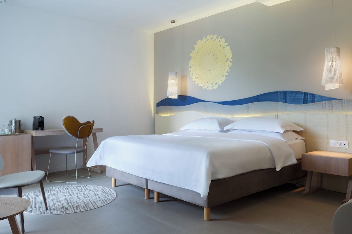 A modern hotel room with a bed, a desk, a chair, and a small table.