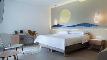 A modern hotel room with a bed, a desk, a chair, and a small table.