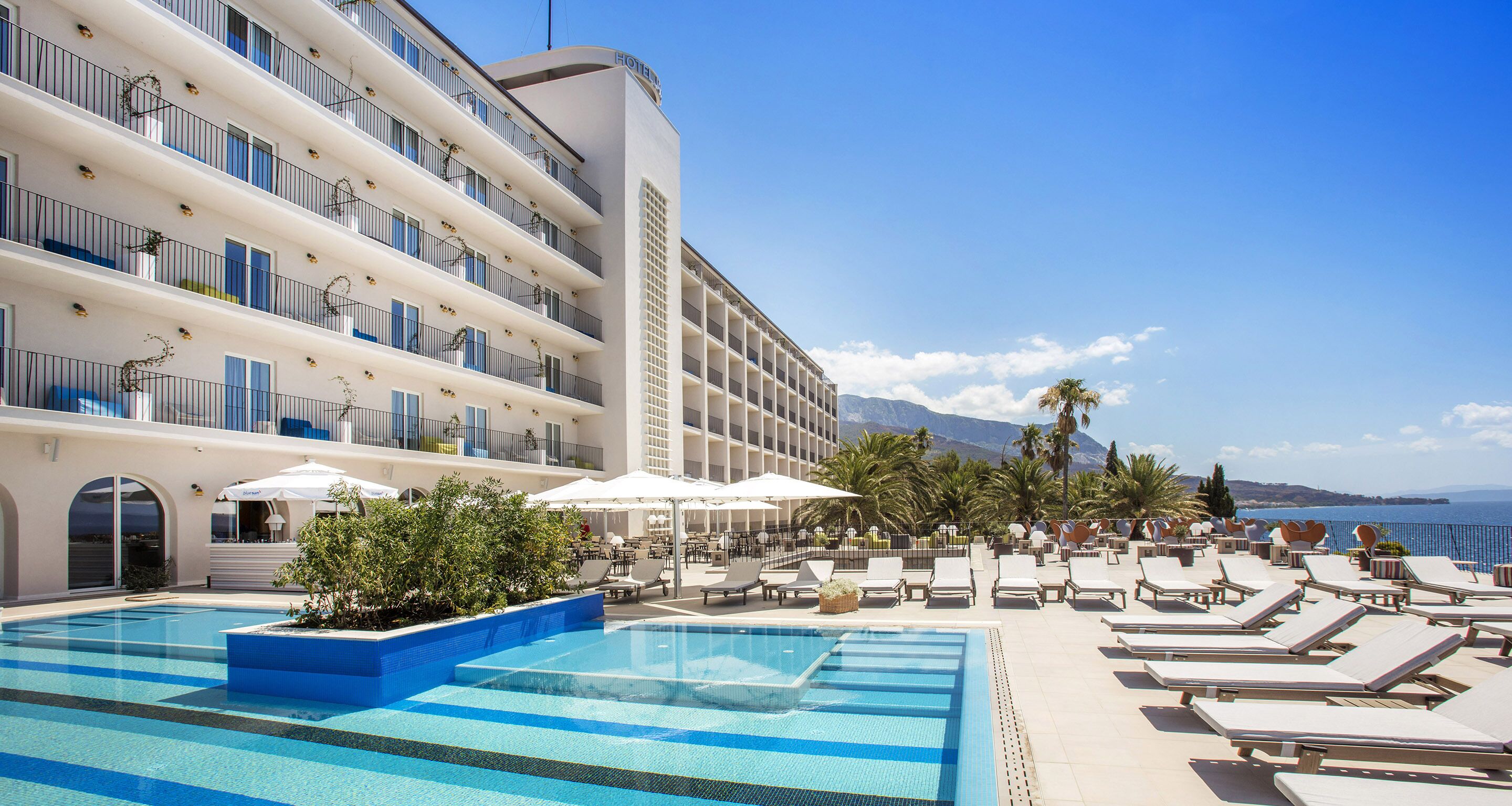 Un hôtel doté d’une piscine, de chaises longues, de parasols et offrant une vue sur la mer.